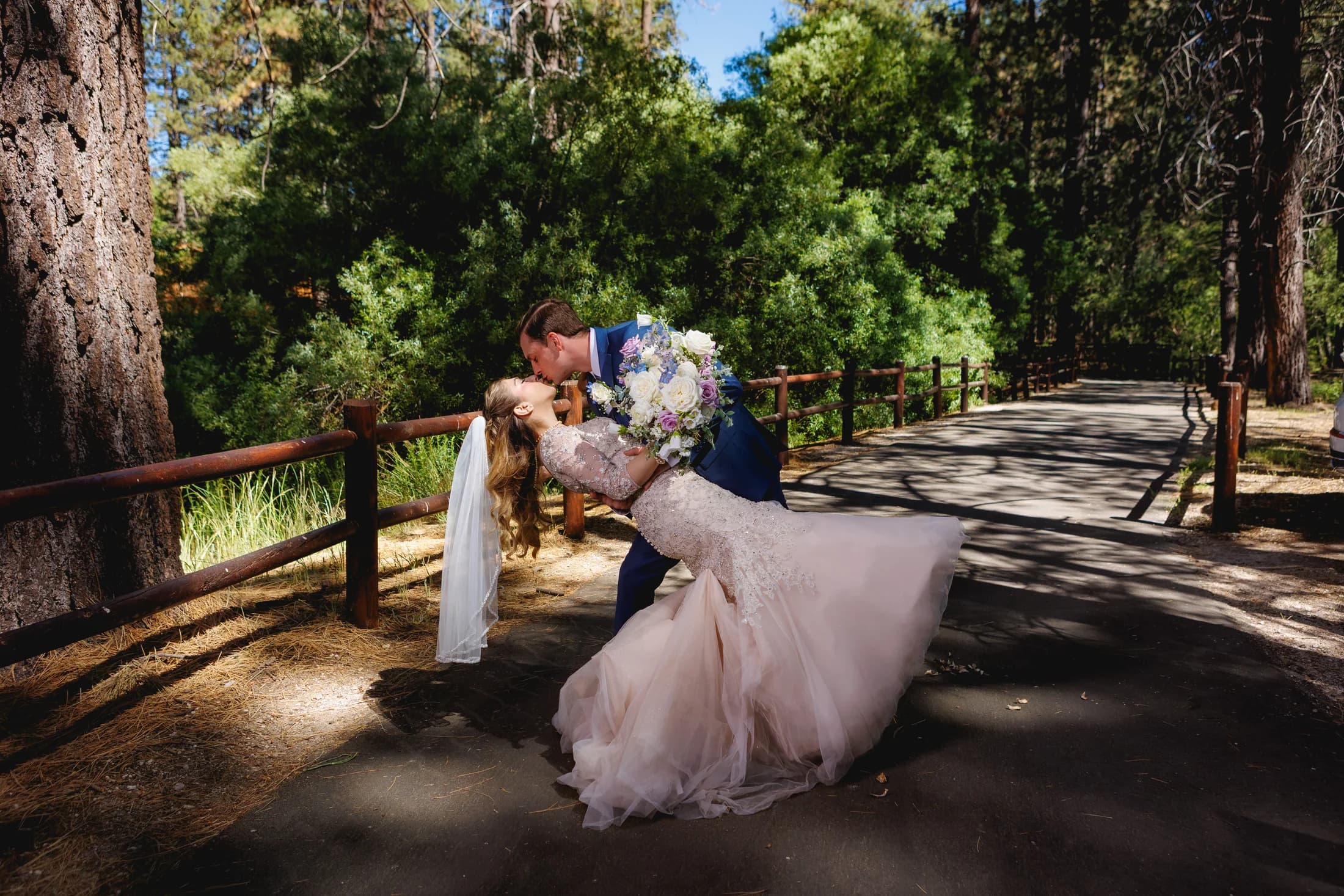 Gloria and Ryan kissing beside a wooden fence and pines on their wedding day